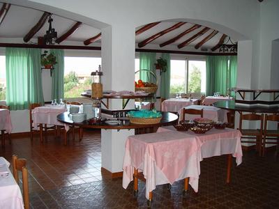 Sala da pranzo con più tavoli, tovaglie rosa e grandi finestre con tende verdi