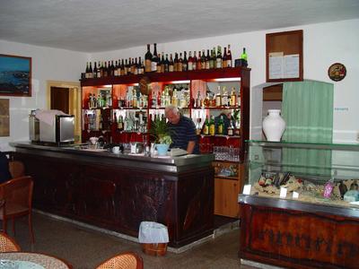 Kleine Bar mit dunklem Holztheken, vielen Flaschen und Vitrine mit Schmuck. Ein Mann steht dahinter.