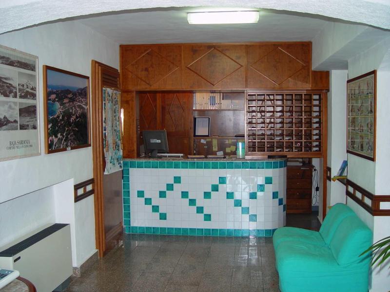 Hell beleuchteter Empfangsbereich mit türkis-weiß gekacheltem Tresen und grünem Sofa rechts.