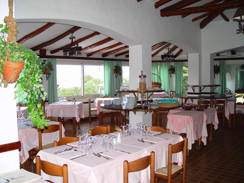 Helles Restaurant mit Holzbalken, weißen Wänden, Tischdecken und Pflanzen an großen Fenstern.