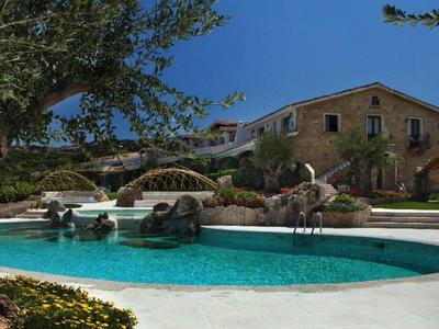 Rustikální hotelová budova s bazénem pod jasnou slunečnou oblohou.