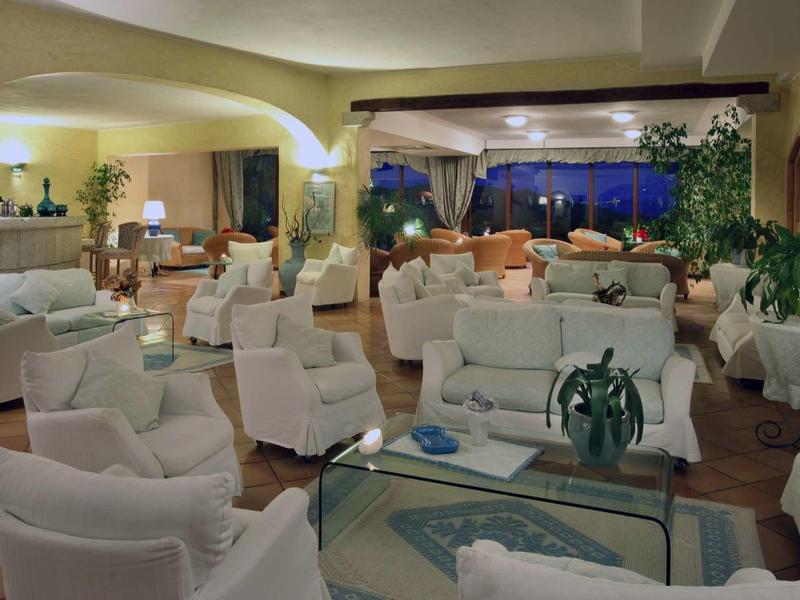 Prostorná hotelová hala s bílými křesly, stoly a nočním výhledem na verandu.