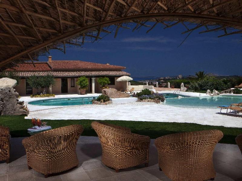 Lounge s ratanovými křesly pod střechou s výhledem na bazén a budovy v noci.