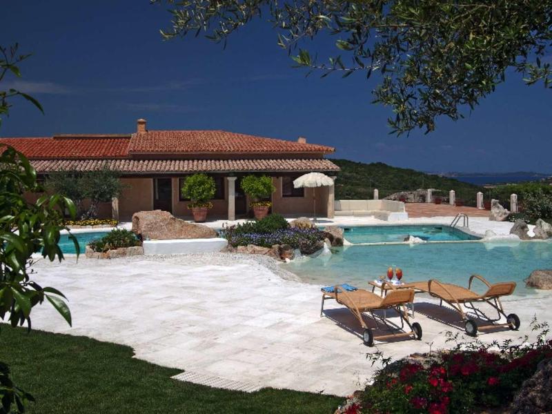 Velký bazén s lehátky a slunečníky vedle budovy pod modrou oblohou.