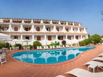 Complesso alberghiero moderno con grande piscina all'aperto e lettini sotto un cielo sereno.