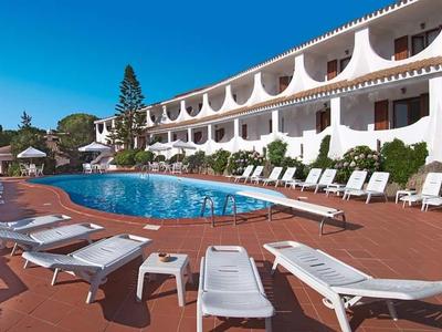 Area piscina moderna dell'hotel con lettini e ombrelloni sotto un cielo blu.