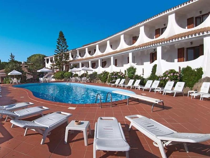 Area piscina moderna dell'hotel con lettini e ombrelloni sotto un cielo blu.