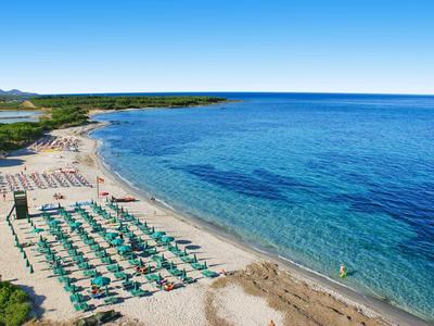 Strand mit Reihen von Liegestühlen und Sonnenschirmen vor klarem, blauem Meer unter hellem Himmel.
