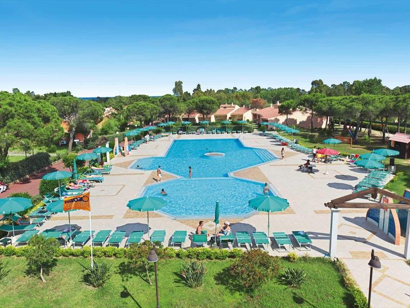 Großer blauer Pool mit Liegestühlen und Sonnenschirmen, umgeben von grüner Gartenlandschaft.