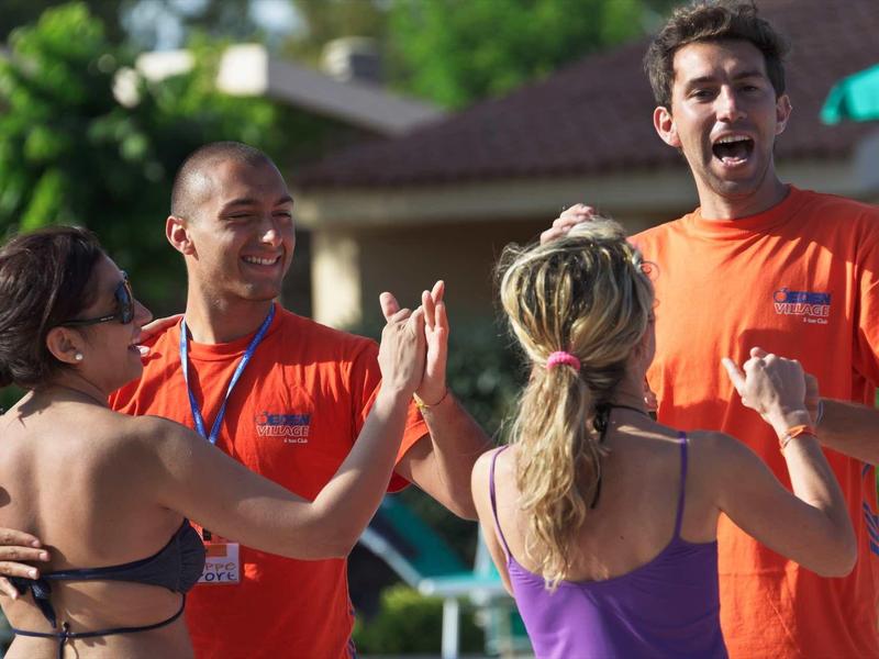 Vier Personen, zwei Männer in orange T-Shirts und zwei Frauen, tanzen und lachen draußen.