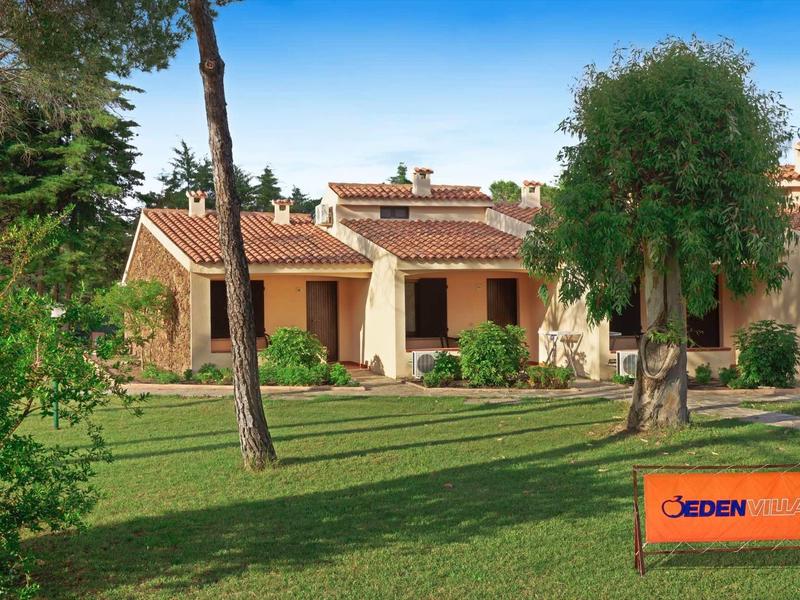 Haus mit roten Ziegeldächern, gelben Wänden, großem grünen Garten und Bäumen im Vordergrund.