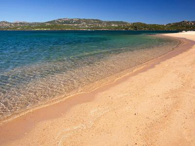 Playa de arena con agua azul clara y colinas verdes al fondo