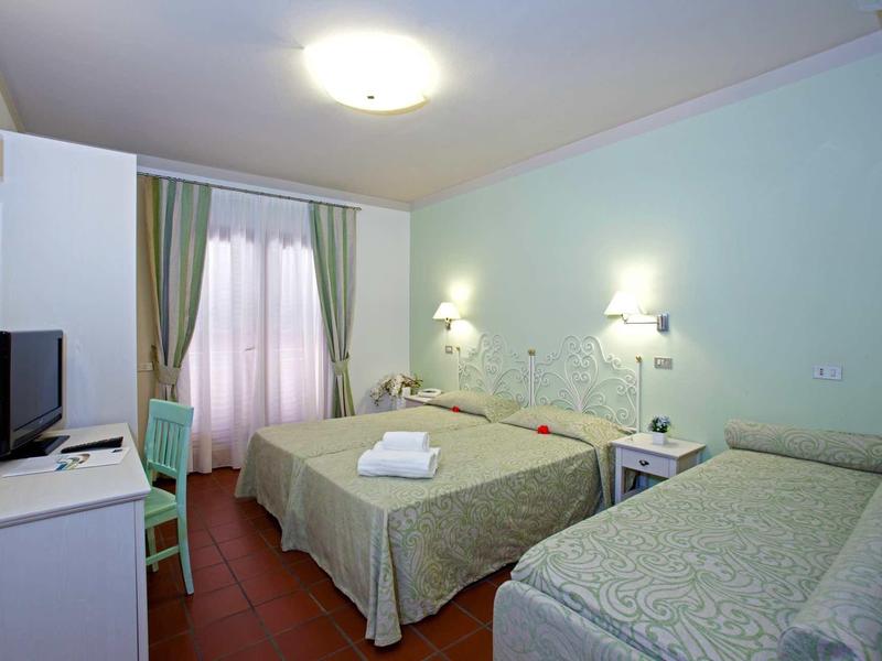 Hotelzimmer mit einem Doppelbett und Einzelbett, weißem Schreibtisch, grünem Stuhl und Vorhängen.