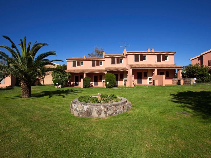 Großes rotes zweistöckiges Haus mit gepflegtem grünen Rasen und Palmen unter blauem Himmel.