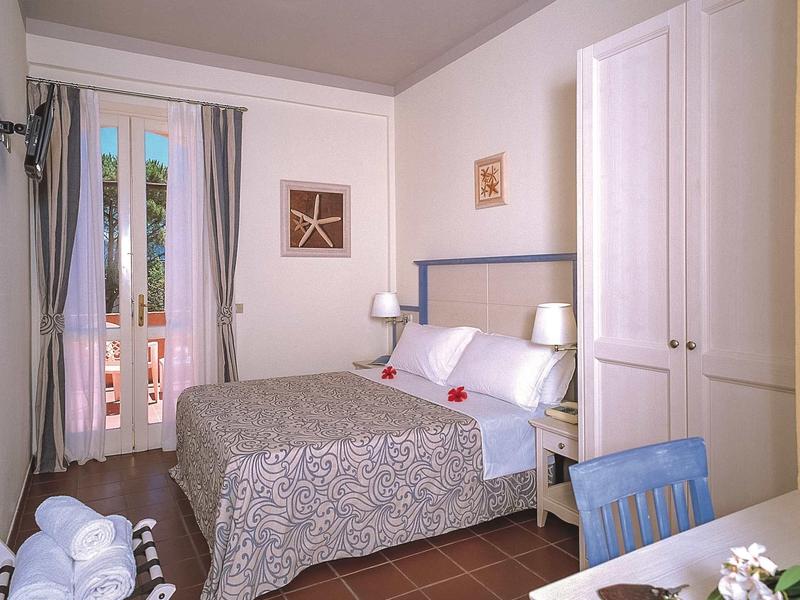 Hell eingerichtetes Schlafzimmer mit großem Bett, Schrank, Tisch mit Stuhl und Terrasse im Hintergrund.