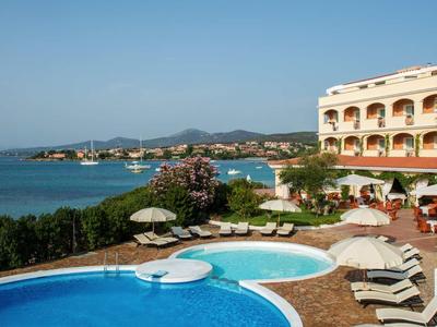 Hotel con piscina e lettini vicino al mare sotto un cielo sereno.