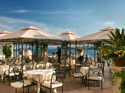 Ristorante all'aperto con tavoli apparecchiati e vista mare in una giornata di sole.