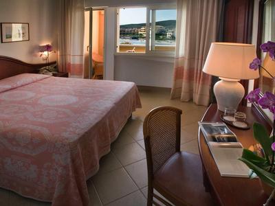 Bedroom with large bed, chair, desk, lamp, and sea view.