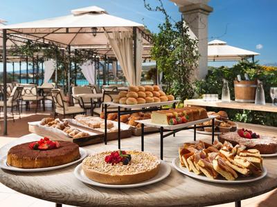 Terrazza soleggiata con tavoli e una selezione di torte e pasticcini su un tavolo rotondo.