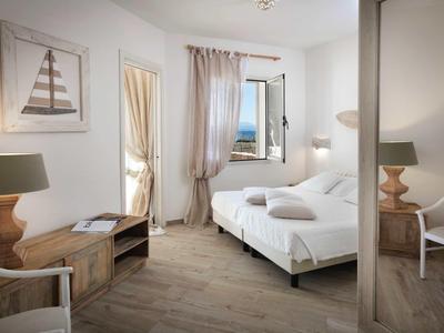 Bright hotel room with double bed, wooden furniture, and sea view through the window.