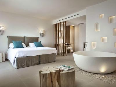 Modern hotel room with double bed, freestanding bathtub, and minimalist design.