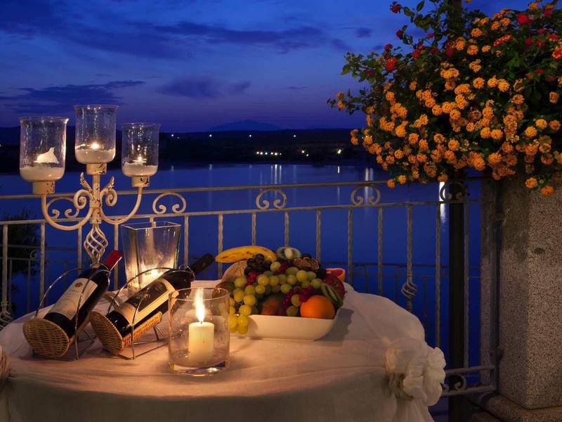 Romantic table with candles, wine, and fruit on balcony overlooking the sea at night.