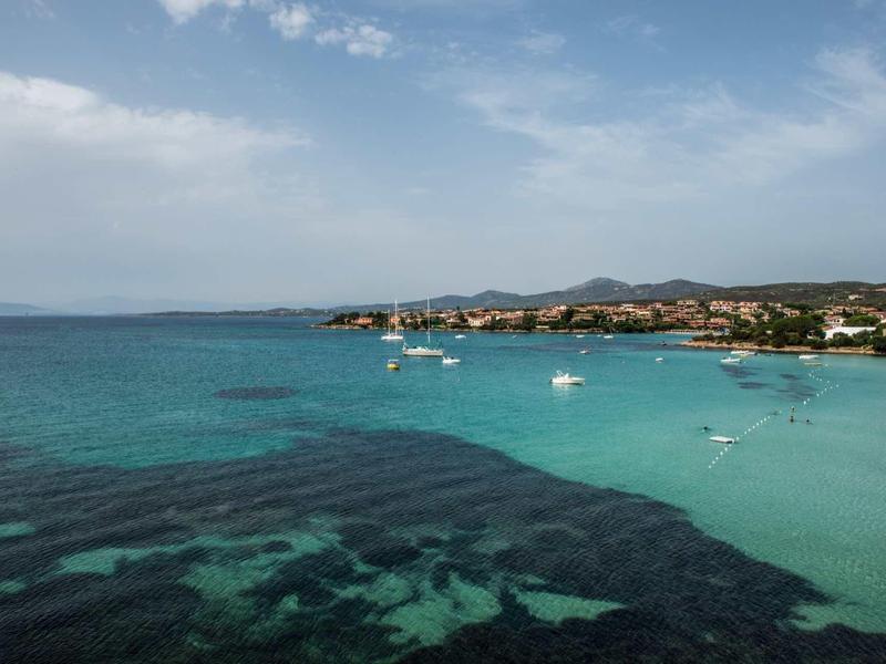 Clear turquoise water with boats and coastal landscape under a cloudy sky.