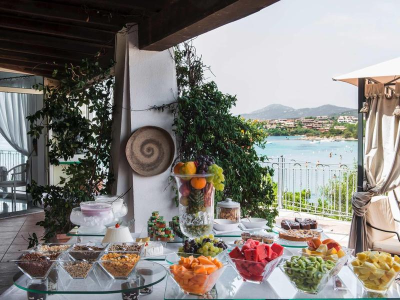 View of a breakfast table with fresh fruit and yogurt on a terrace overlooking the sea.