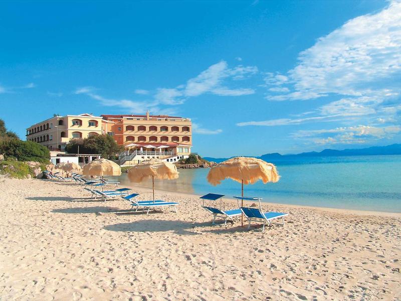 Hotel on the beach with sun loungers and umbrellas under a blue sky.