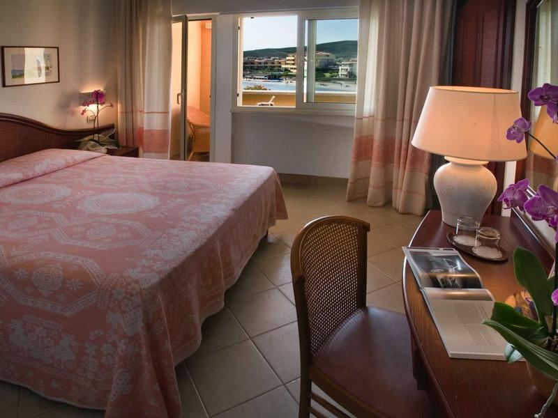 Bedroom with large bed, chair, desk, lamp, and sea view.