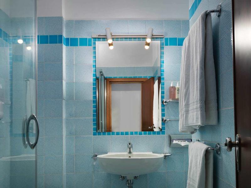 Small bathroom with sink, mirror, blue tiles, and towels.