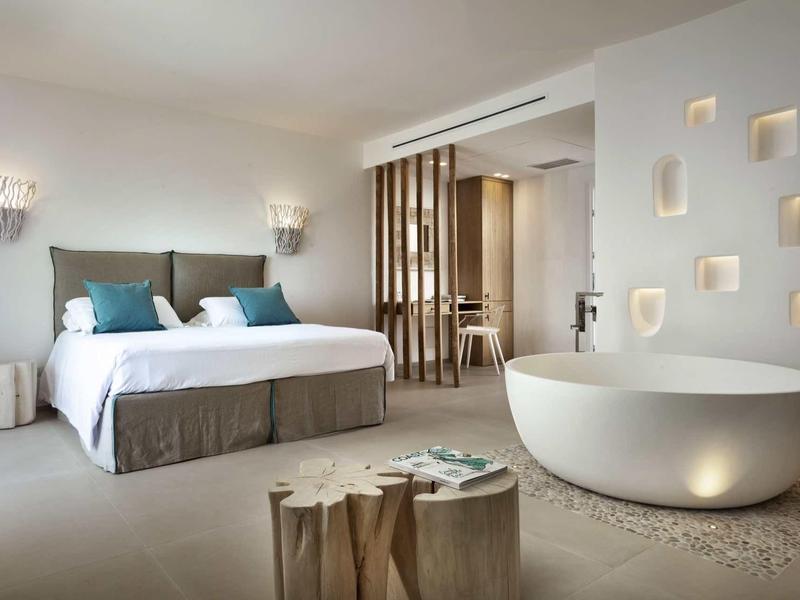 Modern hotel room with double bed, freestanding bathtub, and minimalist design.