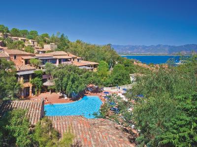 Complesso alberghiero con piscina circondato da alberi verdi e vista sul mare azzurro.