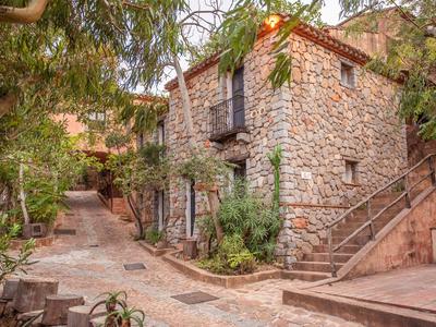 Typický rustikální kamenný dům s balkonem v klidné ulici lemované stromy.