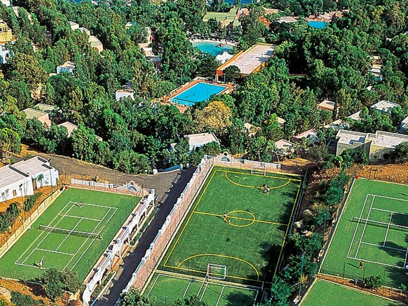 View of a resort with multiple tennis courts and pools in a green hilly landscape.