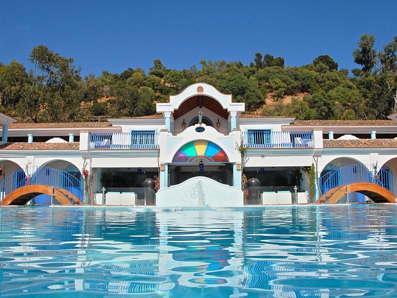 Outdoor pool with slides and sun umbrellas in front of hotel with a hillside backdrop