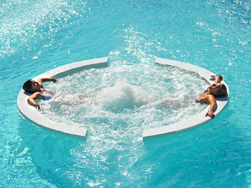 Two people relaxing in a circular swim-up jacuzzi in a clear blue pool.
