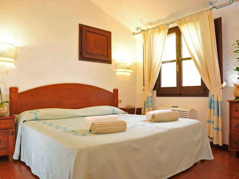 Cozy hotel room with double bed, wooden furniture, white curtains, and warm lighting.