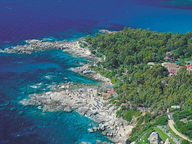 Pobřežní krajina s čistou modrou vodou, kamenitou linií břehu a hustým zeleným lesem.