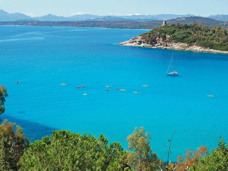 Čisté modré moře s malými loděmi a zalesněným mysím v pozadí.