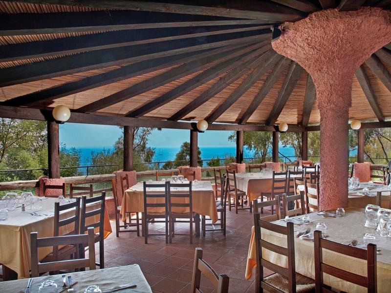 Restaurace pod širým nebem s výhledem na moře, dřevěný nábytek a prostřené stoly venku.