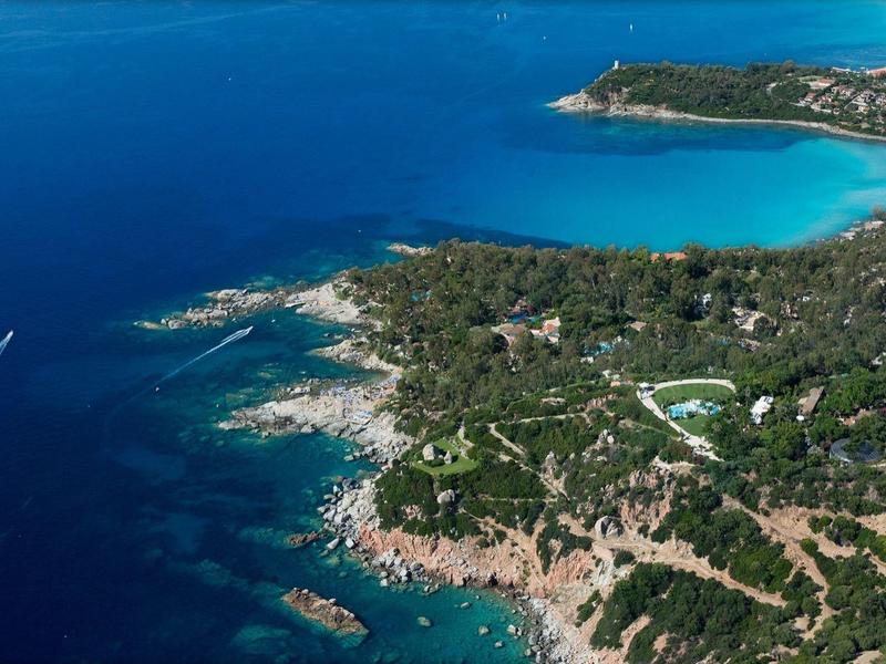 Letecký pohled na zelený poloostrov obklopený modrým mořem s malou pobřežní osadou.