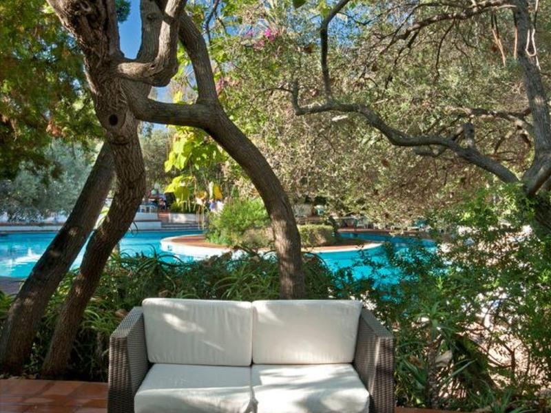 Pohodlná venkovní posezení s pohovkou a stolem vedle bazénu obklopeného stromy.