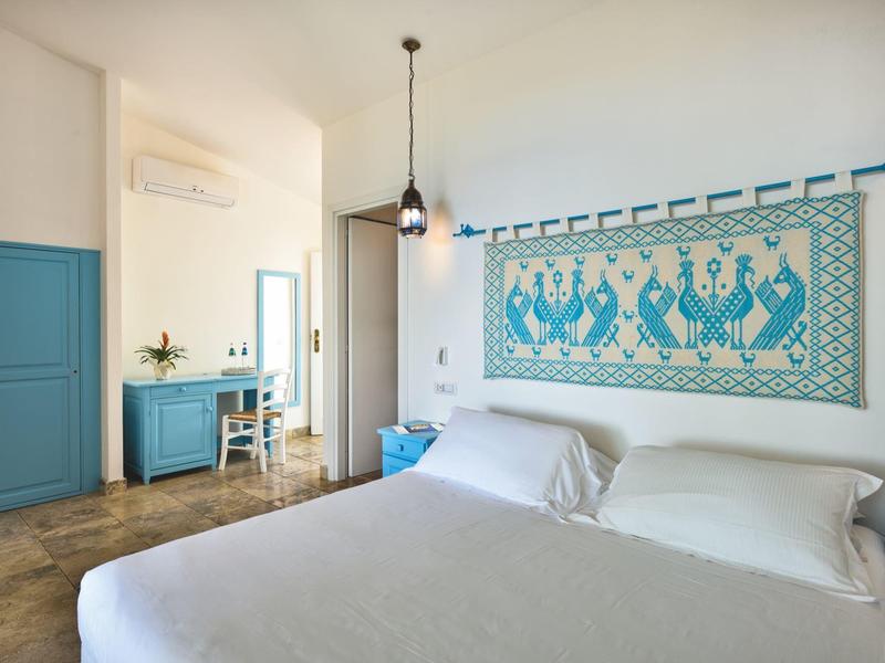 Světý hotelový pokoj s manželskou postelí, modrými akcenty a námořnickou nástěnnou dekorací.