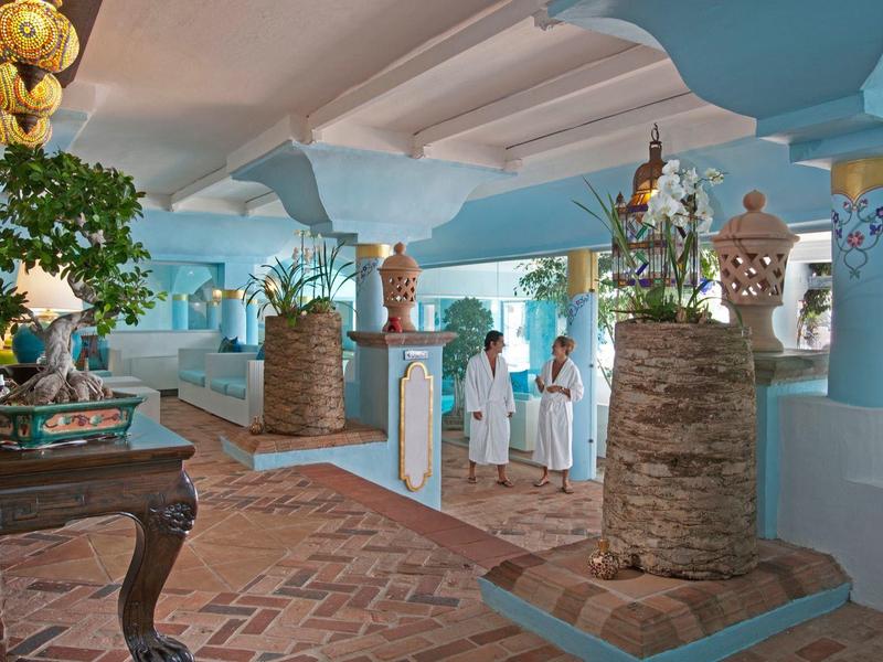 Heller Innenraum mit blauen Säulen, dekorativen Pflanzen und Personen in weißen Kleidung.