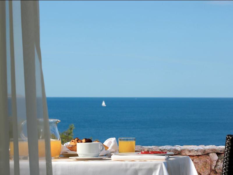 Blick von Balkon mit Frühstückstisch auf blaues Meer und Segelboot am Himmel bei klarem Wetter.