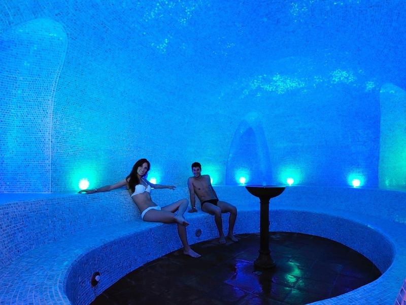 Ein blau beleuchteter runder Whirlpool mit zwei Personen und glatten weißen Wänden.