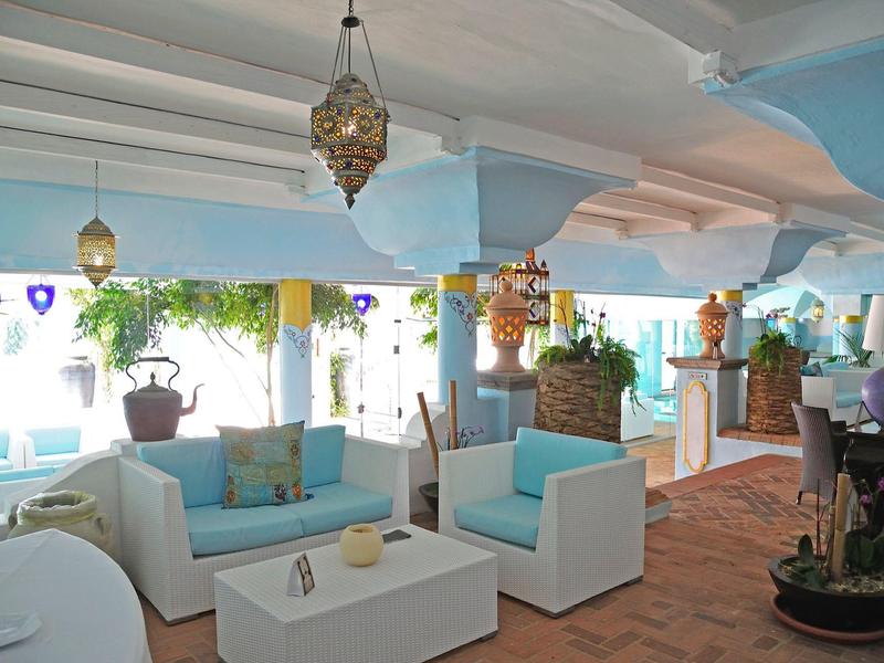 Hell eingerichteter Lounge-Bereich mit weißen Sitzmöbeln, bunten Kissen und hängenden Laternen.