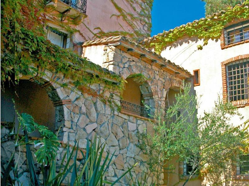 Ein kleines Wasserbecken mit Fontäne vor einer Steinmauer und alten, bepflanzten Gebäuden.