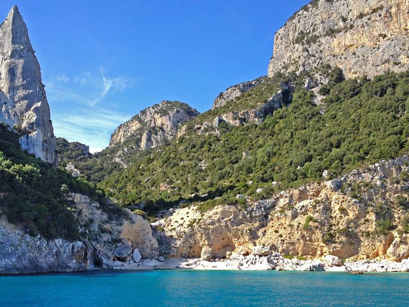 Klares blaues Meer vor felsiger Küste mit steilen Klippen und bewachsenen Hügeln.